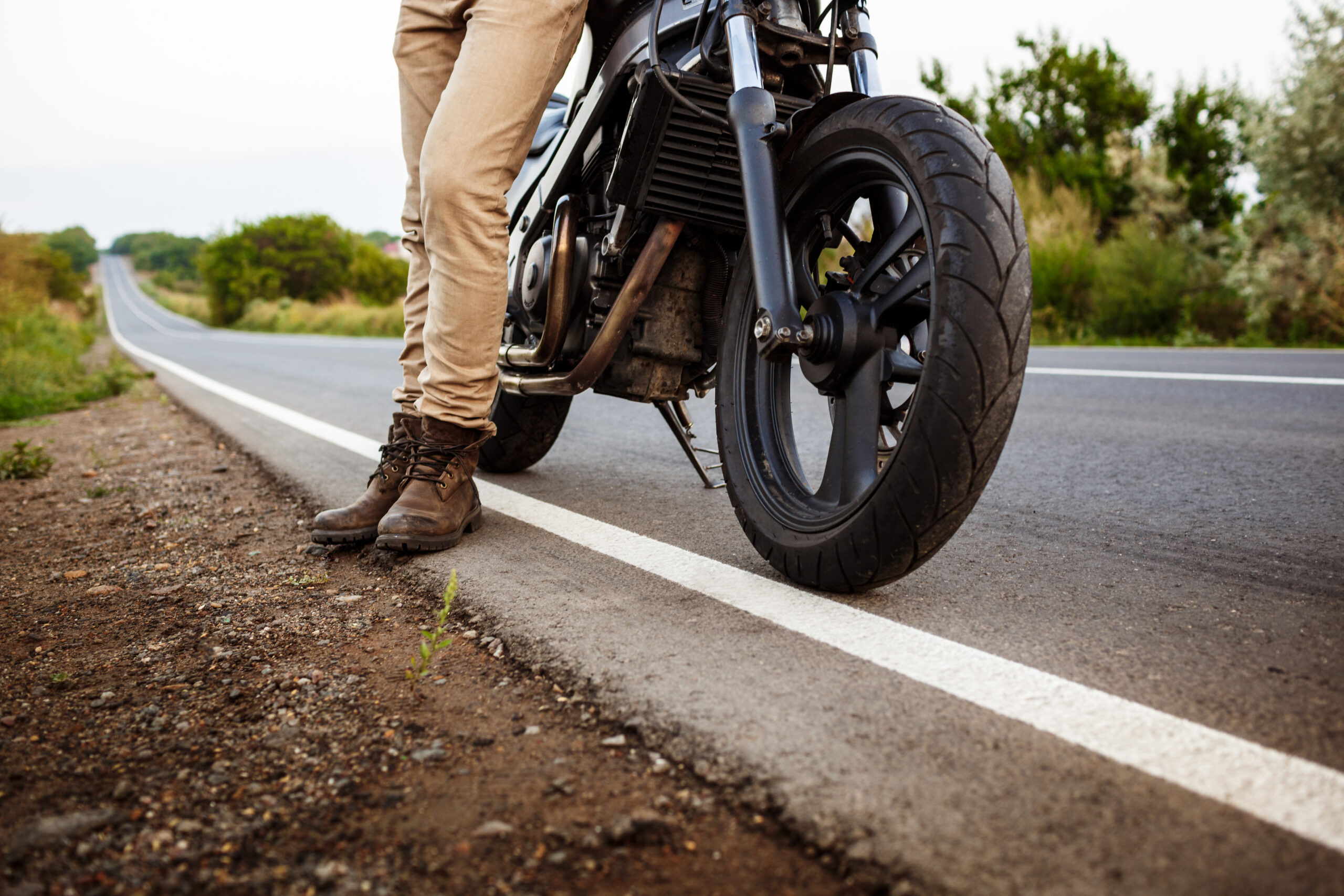 Young handsome man in black leather jacket posing near his motorbike at countryside road.